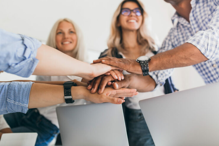 Blonde female office worker looking up with smile while holding hands with colleagues. Indoor portrait of friends ready to start joint work project.. Accompagnement